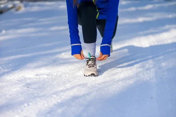 Kar yağışlı kış gününde koşmadan önce çömelmiş ve spor ayakkabılarını düzelten beyaz bir kadın.