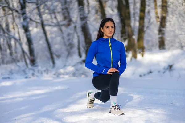 Karlı kış gününde, kusursuz formda, bacağını esneten genç bir sporcu..