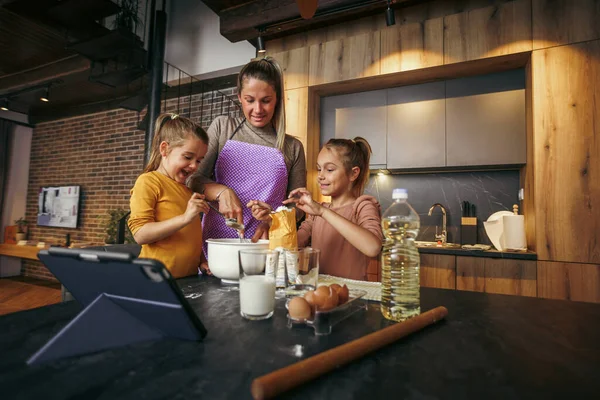 Küçük kız kardeşler mutfakta anneleriyle yemek pişiriyor. Mutlu anneleri olan sevimli çocuklar akşam yemeği veya yemek hazırlıyorlar..