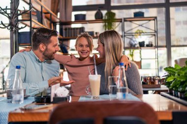Lokantada öğle yemeklerini beklerken anne, baba ve küçük kızları arasında çok hoş bir kucaklaşma anı. Aile zamanı kavramı.