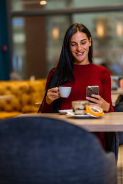 Telefonuna gülümseyen ve kahve içen bir kadın. Kahve molasında mesajlaşan bir kadın.