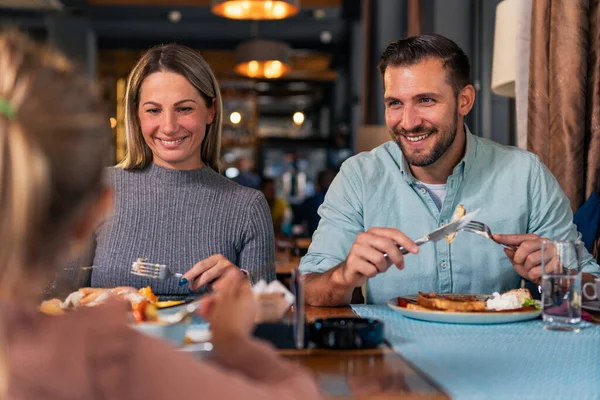 Genç evli çift, küçük kızlarıyla restoranda eğlenceli bir öğle yemeği yiyor..