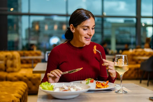 Kırmızı elbiseli çekici esmer, öğle yemeğinden bir ısırık alıyor, şehir manzaralı bir restoranda makarna yiyor.