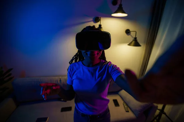 Excited girl wearing virtual reality headset in neon light trying to touch what she sees