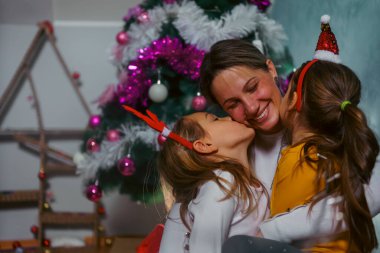 Anne ve iki kız Noel ağacının önünde birbirlerine karşı sevgi besliyorlar. Sıcak bir tatil sezonu ve çok eğleniyorlar.