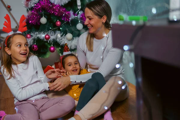 Mutlu bir aile Noel tatilinde eğleniyor, birbirine eşlik ediyor, oturma odasında Noel ağacının önünde oturuyor.