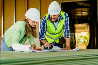 Kadın mimar ve erkek müteahhit inşaat alanının planlarını inceliyor..