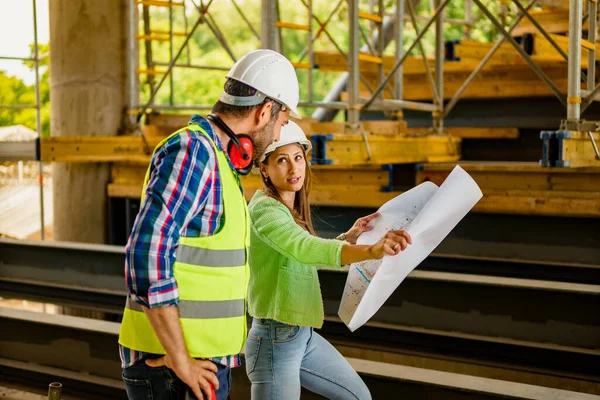 Kadın mimar inşaat alanındaki yöneticiye planı açıklıyor. Mühendis müteahhitle konuşuyor..