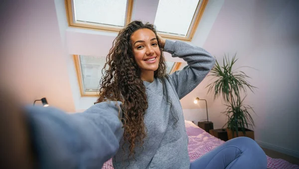 Kıvırcık saçlı güzel bir kadının portresi, gülümsüyor ve mutlu, yatağında oturuyor.