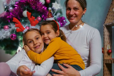 Anne ve iki kızı Noel ağacının önünde poz veriyorlar. Sıcak bir tatil sezonu ve çok eğleniyorlar.