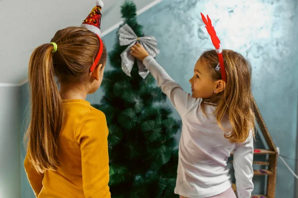 Kız kardeşler Noel ağacını oturma odalarında süslüyor, eğlenceli saç bantları takıyorlar.