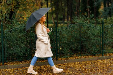 Sonbahar günü yağmurda siyah şemsiyeli bej bir ceket giyen bir kız.