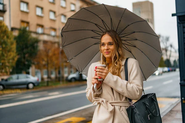 Bulutlu bir gün, sonbaharda yağmurlu bir hava Bir kadın sıcak kahve fincanını tutuyor Toplu taşımayı beklerken