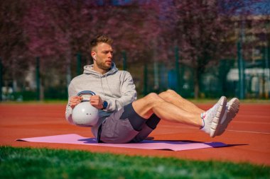 Genç kaslı adam dışarıda kettlebell ile egzersiz yapıyor. Ağırlık kaldırma egzersizi. Spor, spor konsepti.