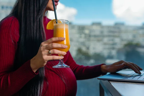 Hamile bir kadının karnının ve portakal suyunun kapanması ve e-kitap okuması. Hamile kadın taze portakal suyundan hoşlanıyor.