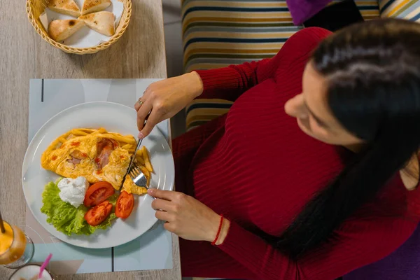 Lokantada kahvaltı yapan hamile bir kadının yakın çekimi. Kahvaltıda yumurta ve domates yiyen kadın.