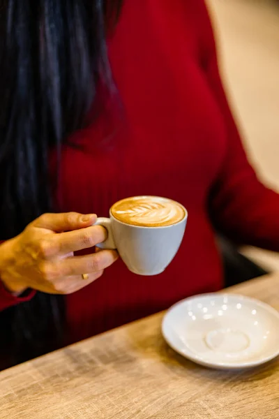 Closeup of a woman holding a coffee cup. Woman holding a latte in a white coffee cup with a leaf design