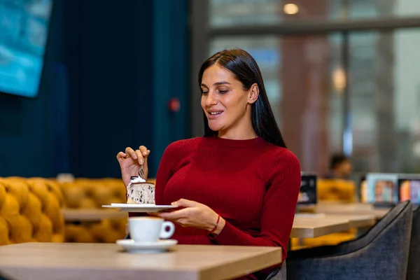 Pregnant woman eats cake in a cafe, drinks some coffee . Beautiful woman in a red dress eating oreo cake - chocolate cake after long day at work