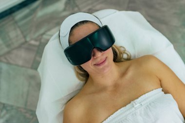 Kadın lazer tüy aldırmaya hazırlanıyor. Koruyucu gözlük takıyor.