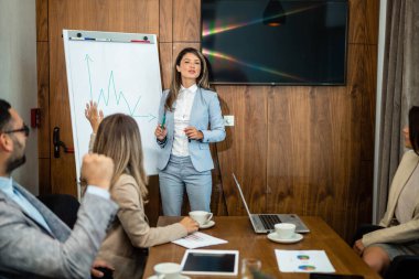 Young Caucasian female coach or speaker make whiteboard presentation for diverse employees in office, focused biracial woman trainer present business project on flip chart at meeting