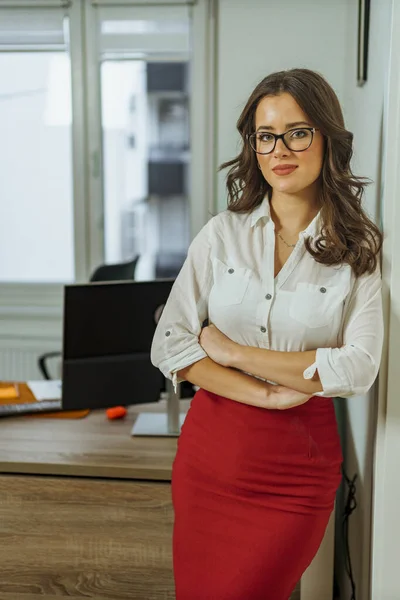 Güzel genç kadın kameraya gülümsüyor, esmer, kıvırcık saçlı ve gözlüklü profil fotoğrafı ve iş profiliyle bağlantılı olarak poz veriyor.