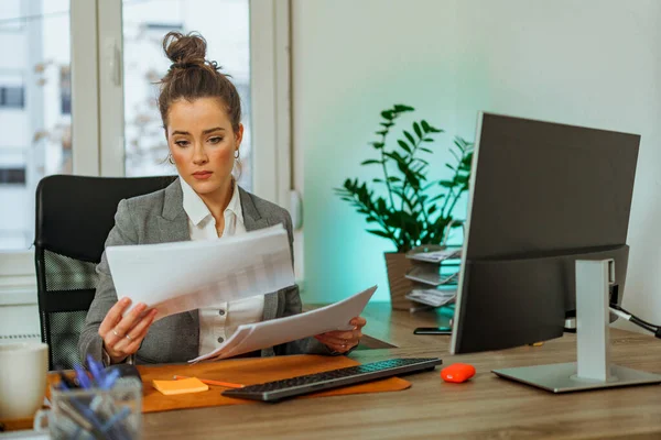 Young woman is sitting at her desk and reading a report on her finance as she gets ready for a meeting with her CEO