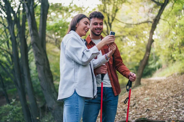 A girl is showing something exhilarating to her boyfriend on her smart phone, and he is enjoying it. Everywhere around them is wonderful greenery.