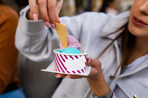 A girl is holding a delicious ice cream in her hands with yummy turquoise and pink scoops.