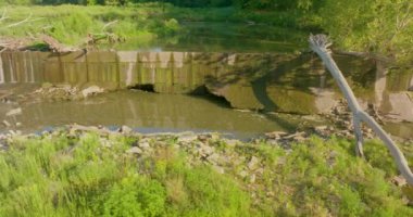 Barajın üzerinden yavaşça akan sığ bir nehir var. Kamera sağdan sola hareket ediyor..