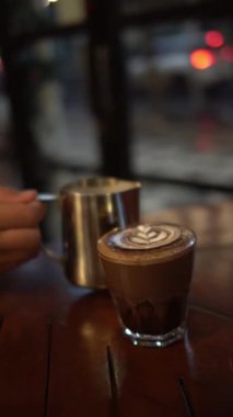 Bir bardak sıcak latte, köpüklü ve arka planda.