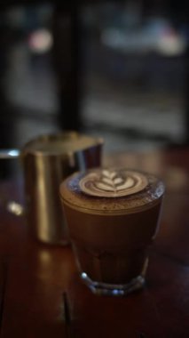 Bir bardak sıcak latte, köpüklü ve arka planda.