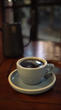 Bir fincan sıcak kahve ya da ahşap masa ve arka planda çay.