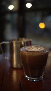 Bir bardak sıcak latte, köpüklü ve arka planda.