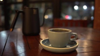 Bir fincan sıcak kahve ya da ahşap masa ve arka planda çay.