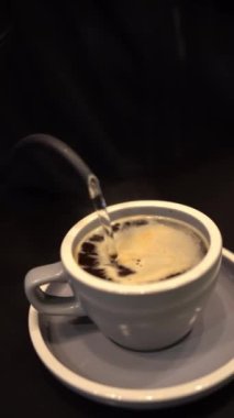 Tezgahta kahve yapmak için bardağa sıcak su döken biri.