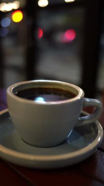 Bir fincan sıcak kahveyi ya da çayı, arka planda bokeh olan ahşap masaya koy.