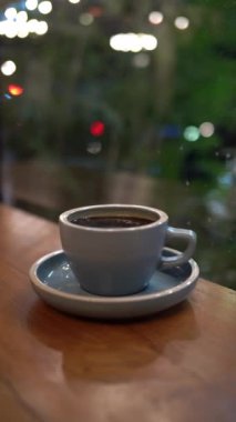 Cam pencerenin yakınındaki tahta masada bir fincan sıcak kahve ya da çay.