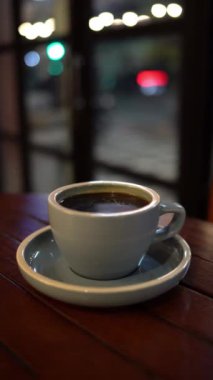 Cam pencerenin yakınındaki tahta masada bir fincan sıcak kahve ya da çay.