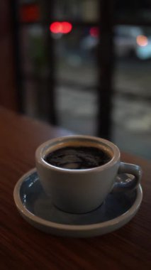 Cam pencerenin yakınındaki tahta masada bir fincan sıcak kahve ya da çay.