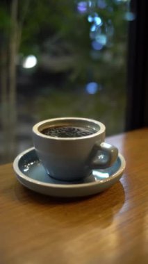 Cam pencerenin yakınındaki tahta masada bir fincan sıcak kahve ya da çay.