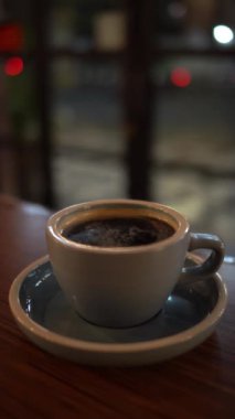 Cam pencerenin yakınındaki tahta masada bir fincan sıcak kahve ya da çay.