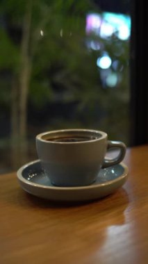 Bir fincan sıcak kahveyi ya da çayı, arka planda bokeh olan ahşap masaya koy.