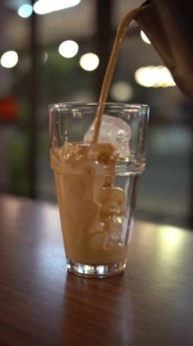 Arka planda bulanıklık olan bir bardak buzlu suya kahve dökmek.