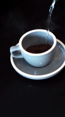 Yüksek açı, kahve yapmak için bardağa sıcak su döken kişinin yakın görüntüsü.