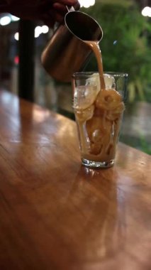 Arka planda bulanıklık olan bir bardak buzun üzerine sütlü kahve dökmek.