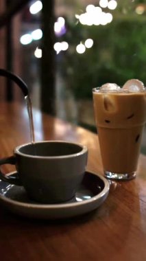 Buzlu kahvenin yanındaki masaya kahve yapmak için bardağa sıcak su döken kişi.