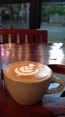 Ahşap masada köpüklü bir fincan sıcak latte.