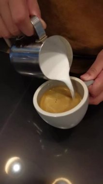 Barista 'nın sıcak sütlü latte bardağında köpük sanatı yaptığı yakın plan.