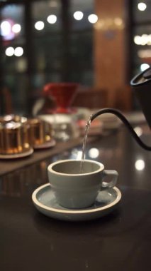 Tezgahta kahve yapmak için bardağa sıcak su döken biri.