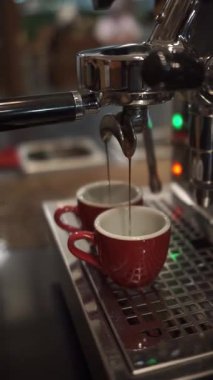 Kahve makinesinden iki kırmızı fincana akan taze espresso görüntülerini kapat.
